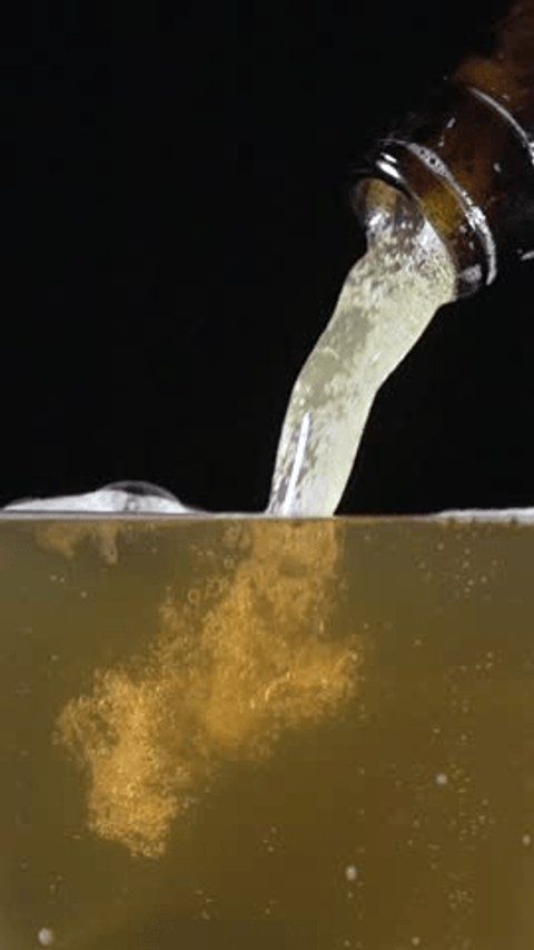 Öl hälls från en flaska ner i ett glas med skum